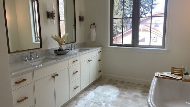 A bright, neutral-toned bathroom featuring a double vanity with brass hardware, dual mirrors, and a freestanding tub.