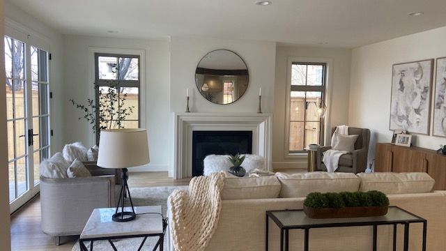 A bright, modern living room featuring a fireplace, a white sofa with a throw blanket, armchairs, and neutral decor.