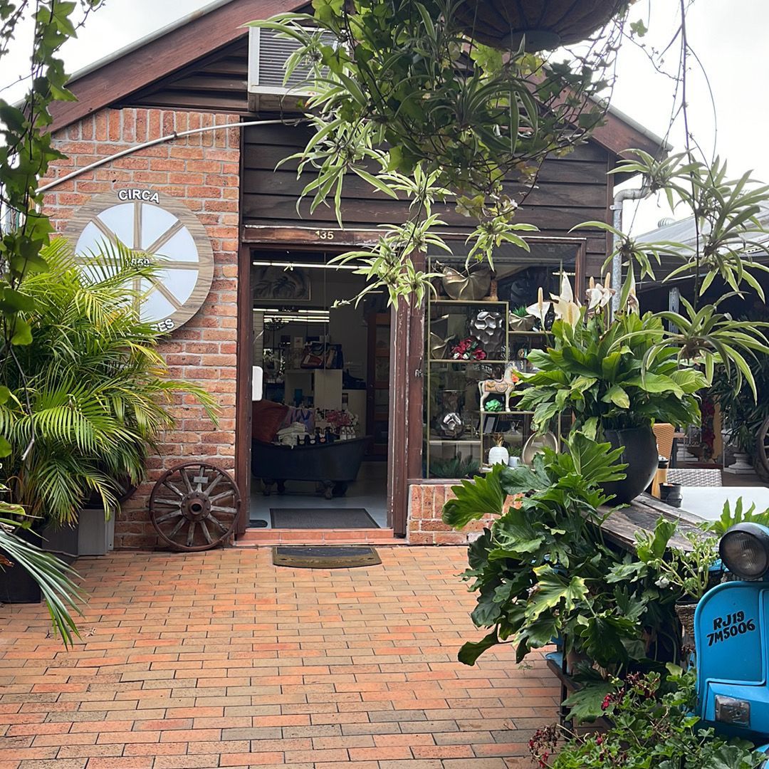 Brick building with open doorway, plants, and decorative wheel.