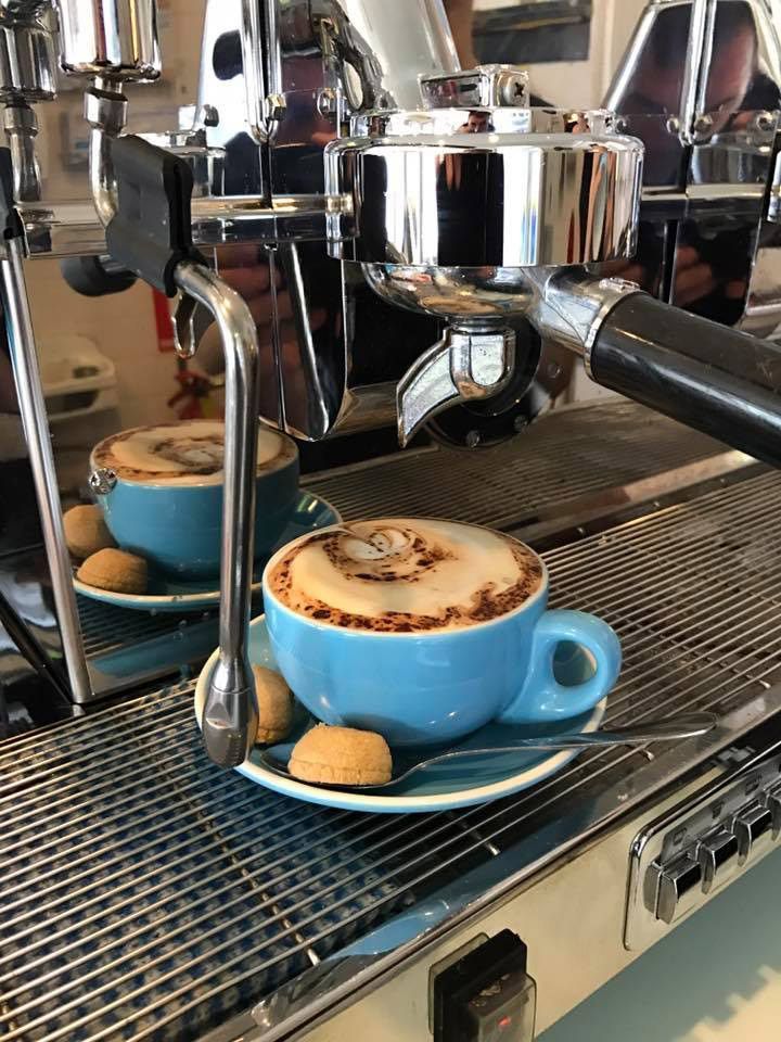 Cappuccino in blue cup on espresso machine with biscotti.
