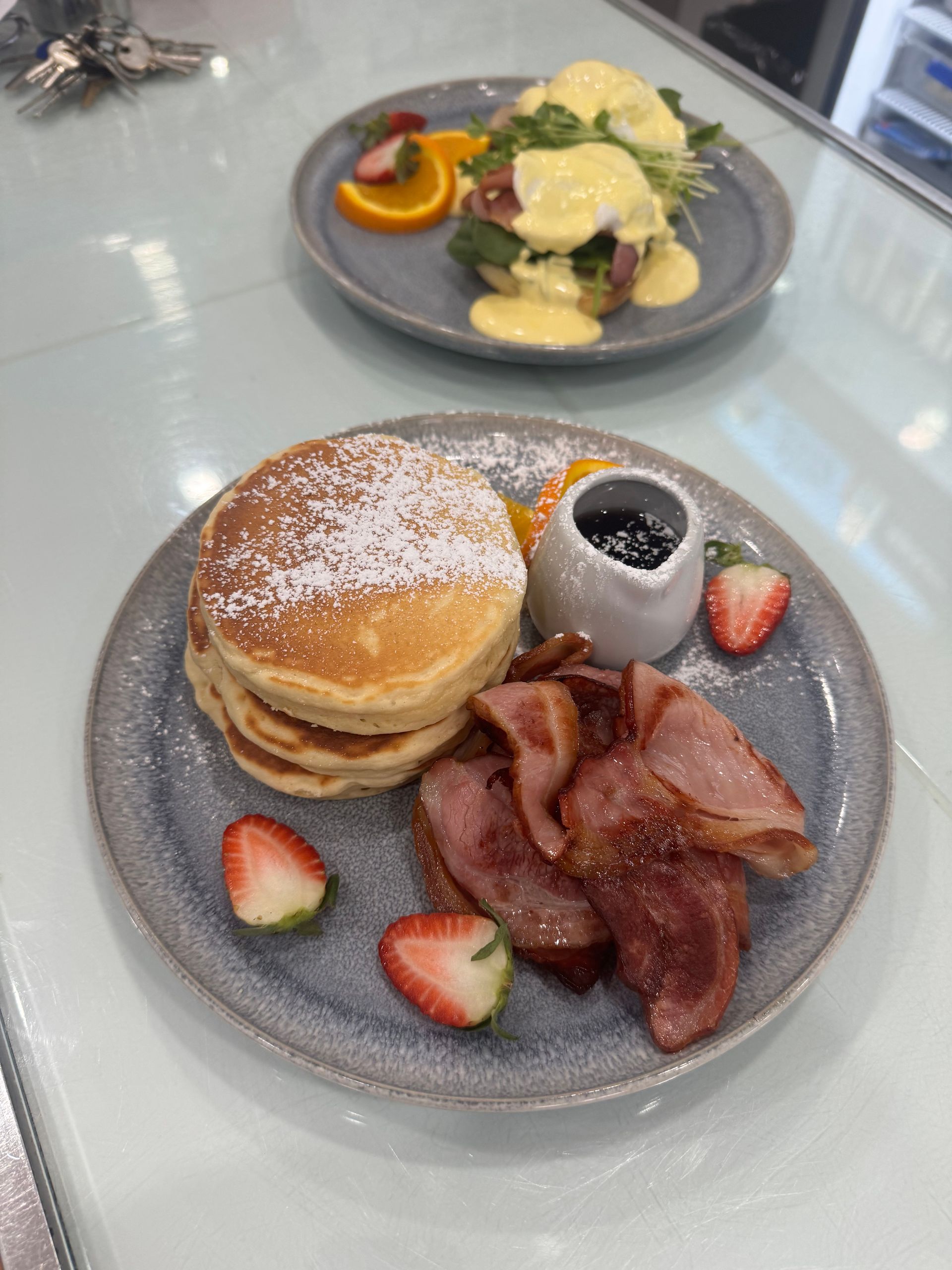 Pancakes with bacon and fruit, and eggs Benedict on grey plates on a table.