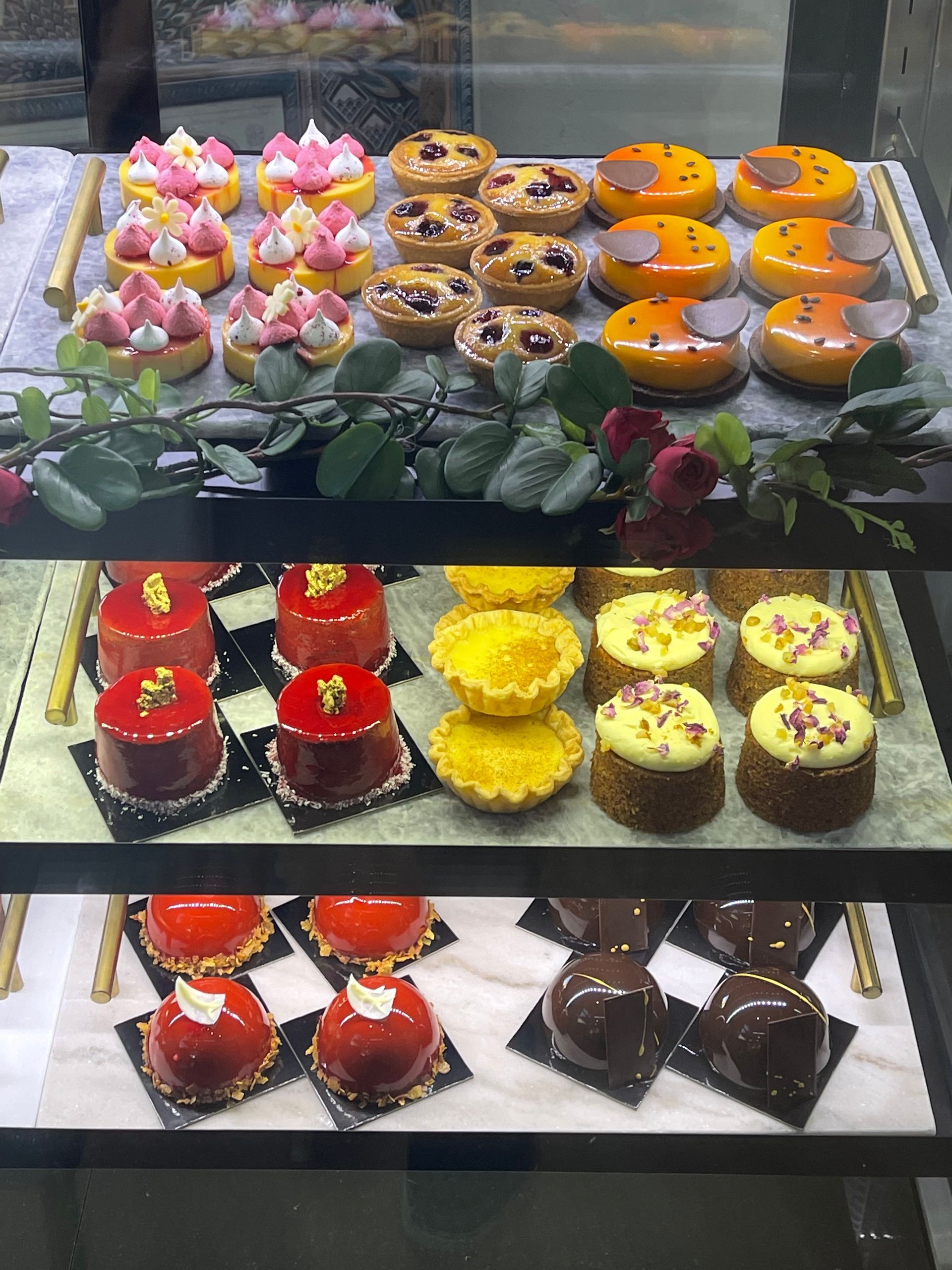 Pastries on display in a glass case, including tarts and small cakes with various colorful toppings.