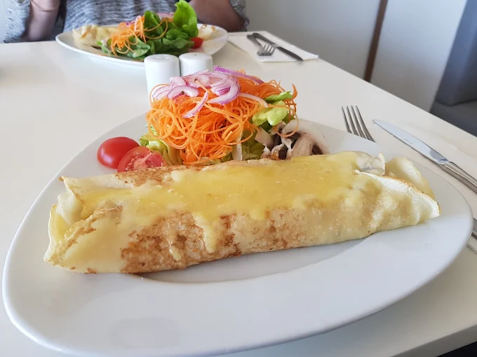 Crepe with cheese, salad with carrots, red onion, tomatoes, and mushrooms on a white plate.