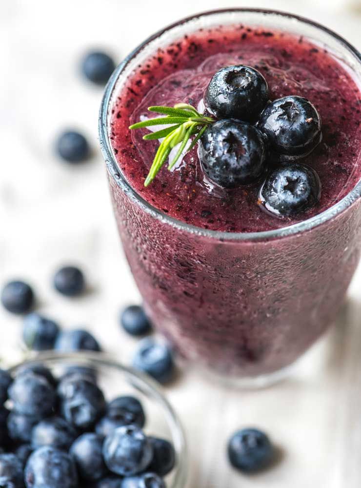 Blueberry smoothie in a glass, garnished with blueberries and rosemary.