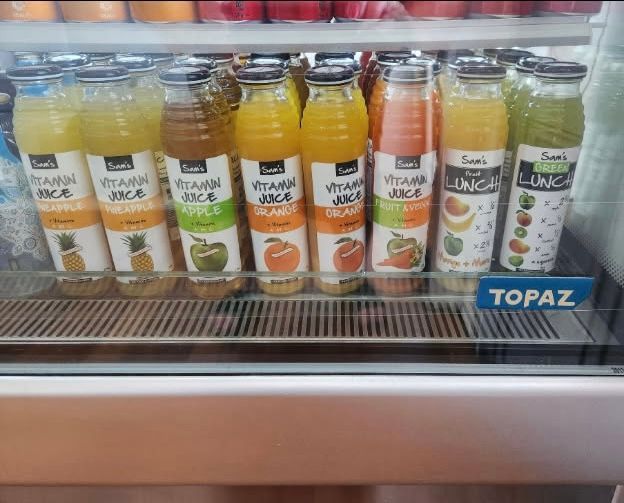 Bottles of fruit juices in a refrigerated display case, variety of colors and flavors.