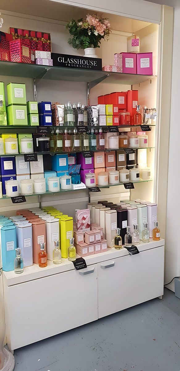 Shelves displaying various candles and perfumes, arranged by color, in a well-lit retail setting.