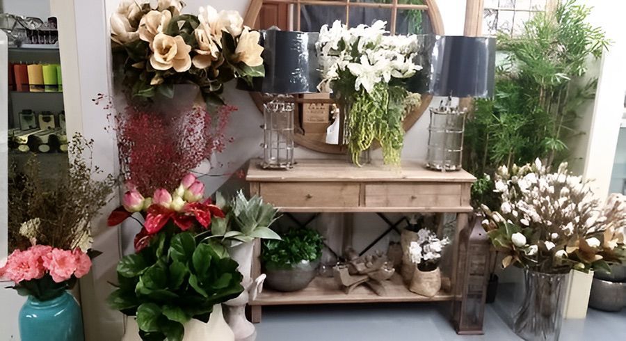A display of flowers and home decor on a wooden table. Lilies, cotton, and lamps are featured.