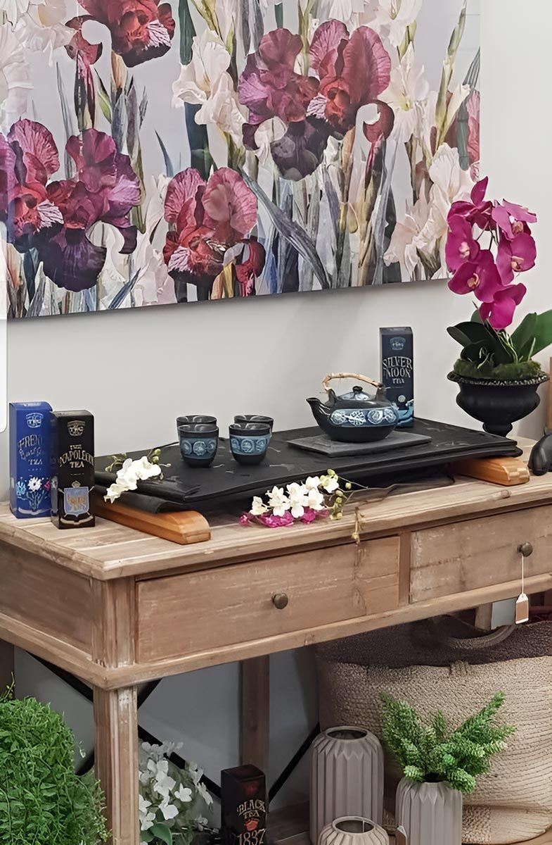 Wooden table with tea set, flowers, and floral artwork.