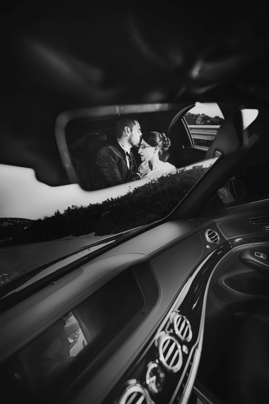 Una sposa e uno sposo si baciano in macchina in una foto in bianco e nero.