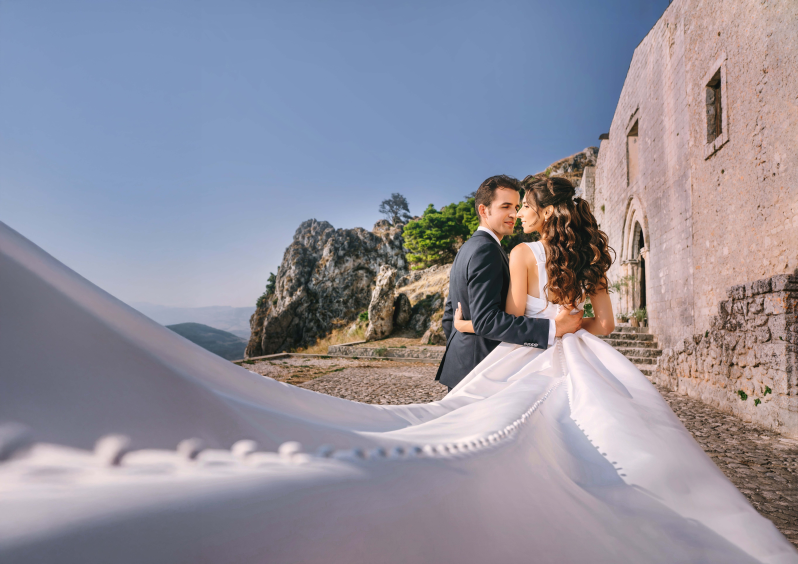 Una coppia di sposi posa per una foto con il loro abito da sposa che svolazza nel vento.
