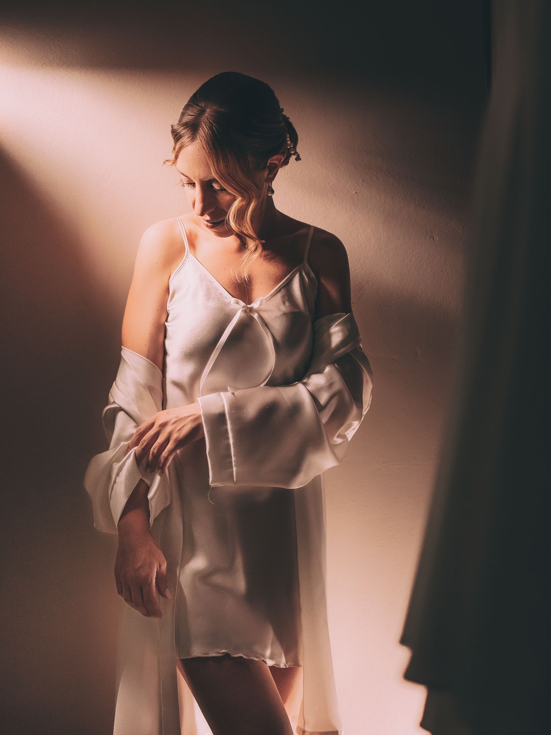 Una donna con un abito bianco e una vestaglia è in piedi in una stanza buia.