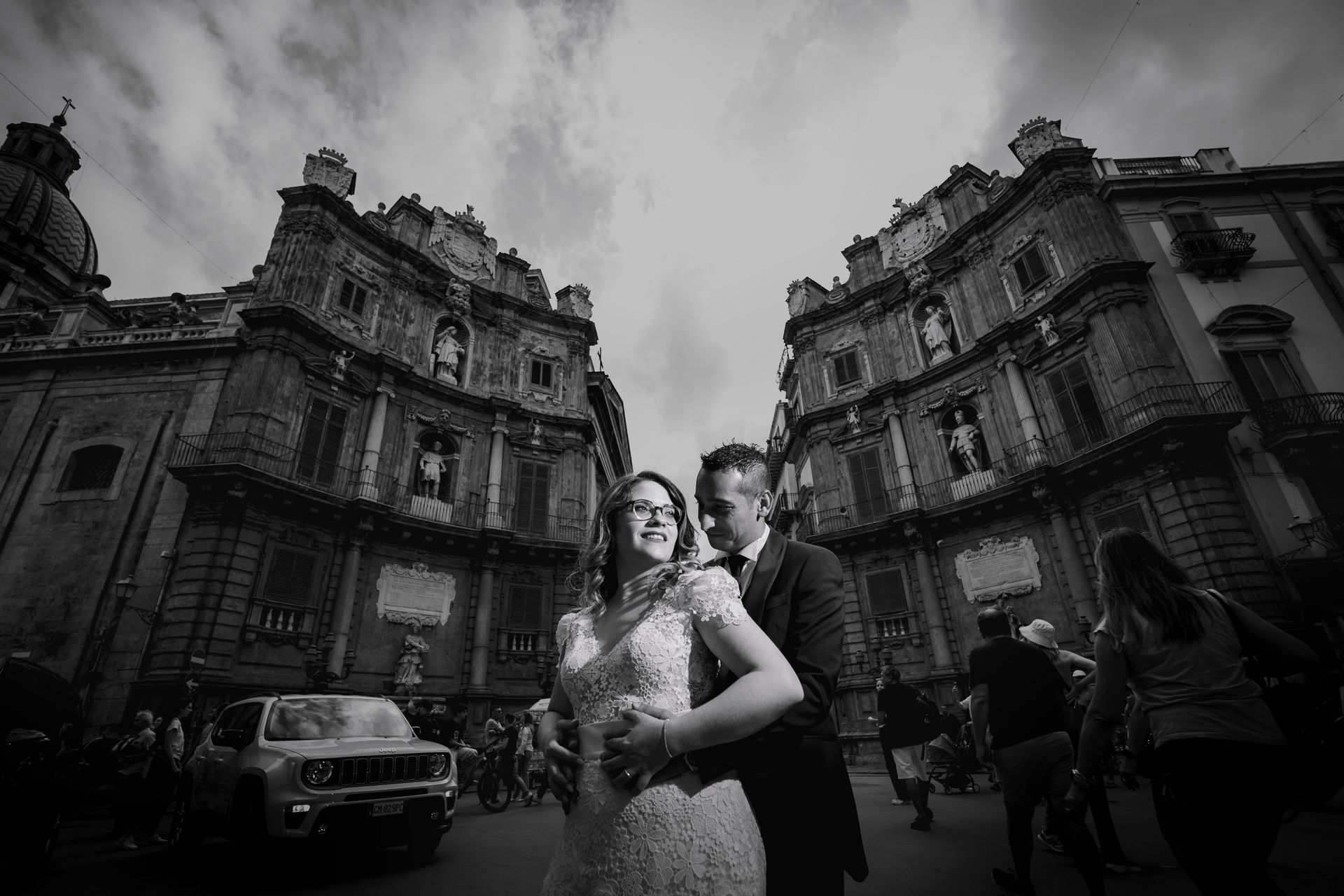 Una foto in bianco e nero di una sposa e uno sposo che ballano davanti a un edificio.