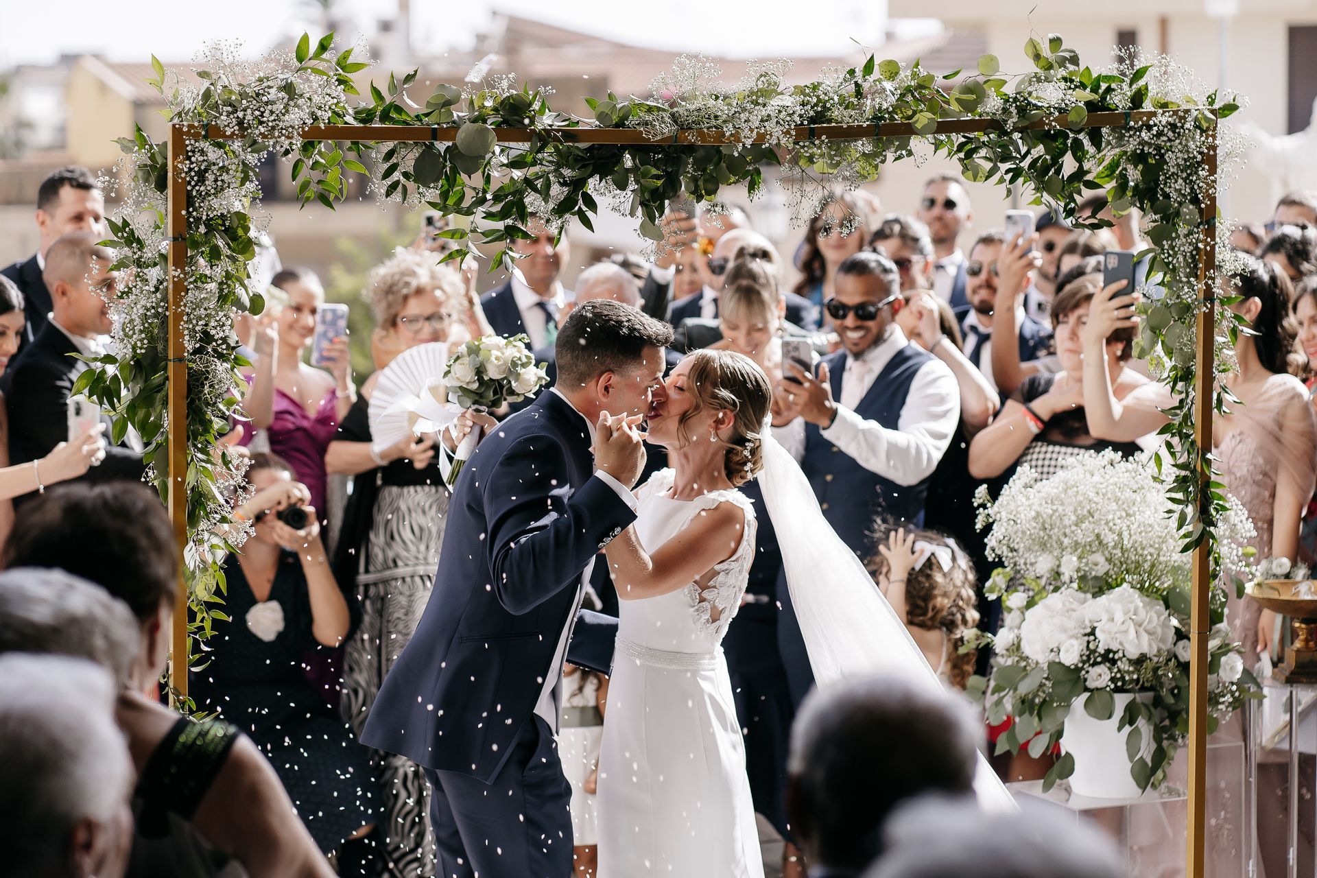 Una coppia di sposi che si baciano davanti agli invitati alle loro nozze.