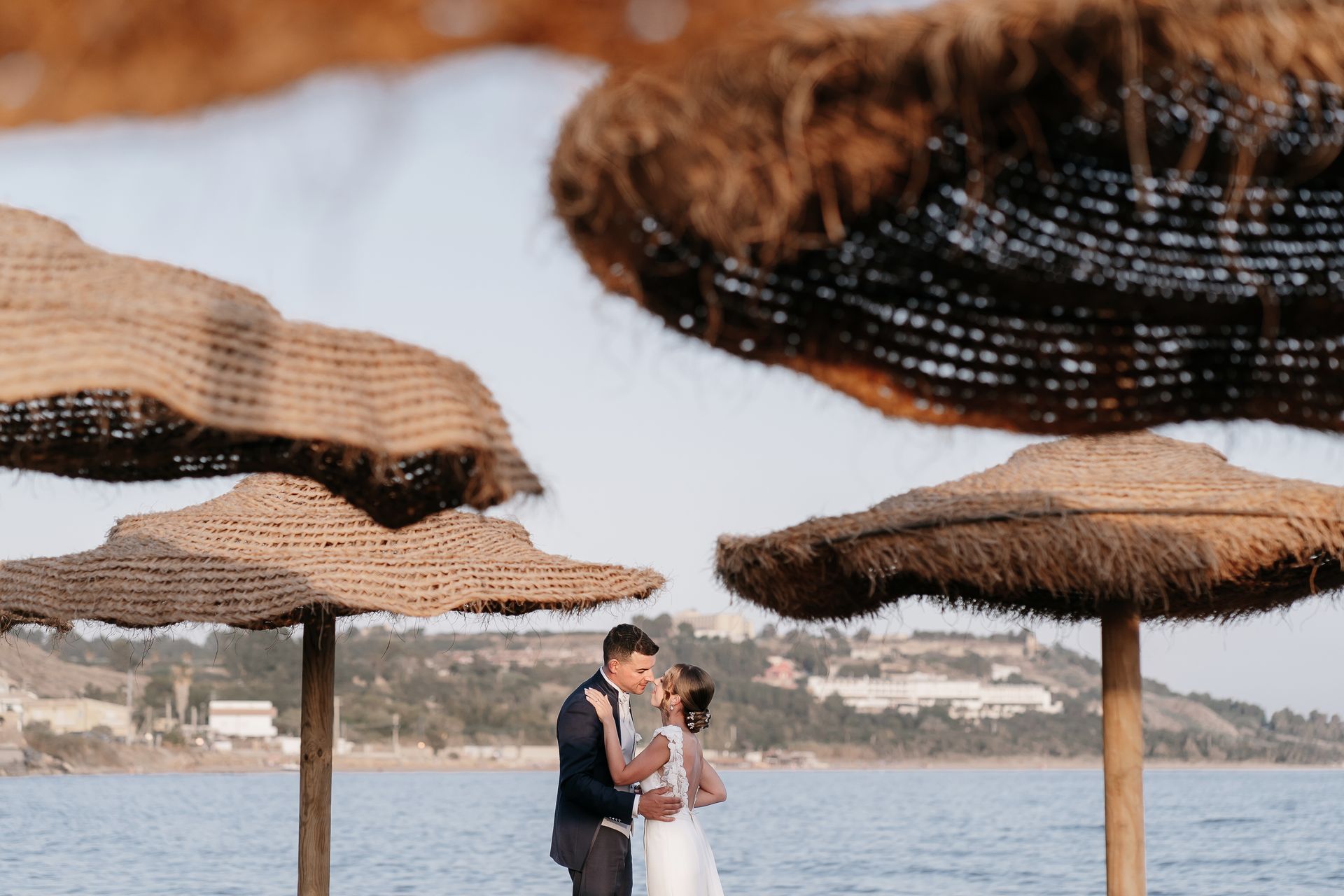 Una coppia di sposi si bacia sotto gli ombrelloni di paglia sulla spiaggia.