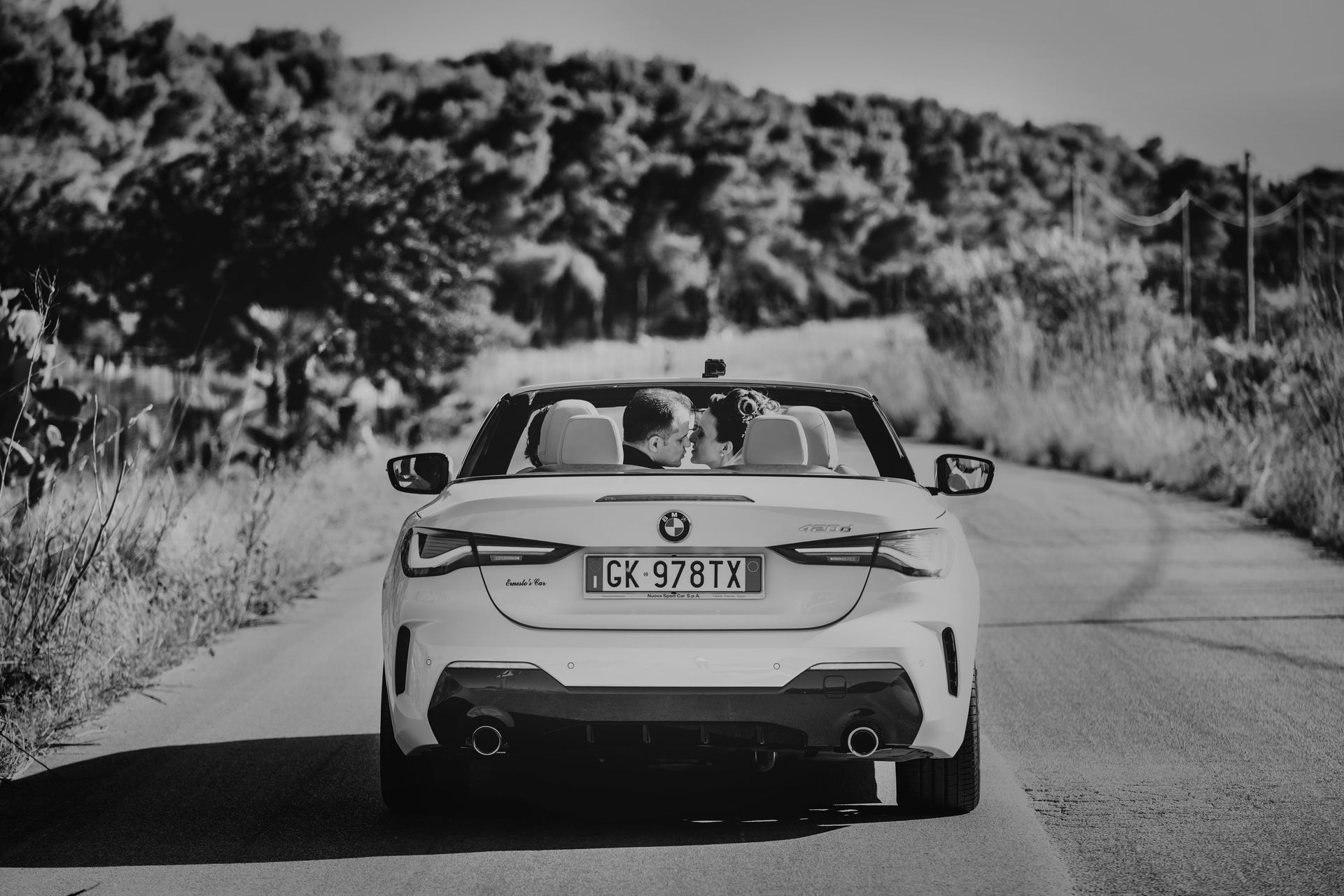 Una foto in bianco e nero di una BMW decappottabile che percorre una strada.