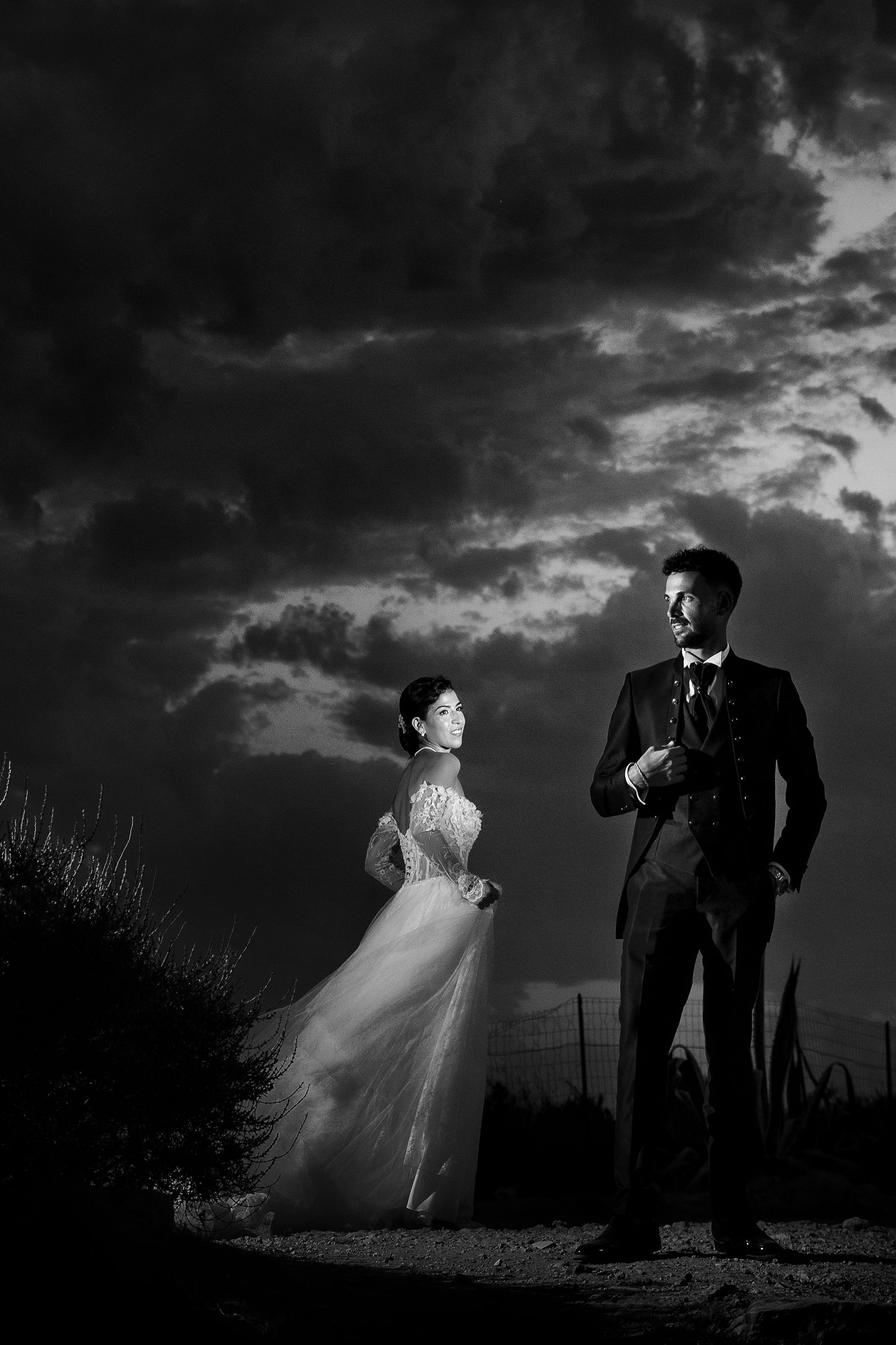 Una sposa e uno sposo sono in piedi uno accanto all'altro davanti a un cielo nuvoloso.