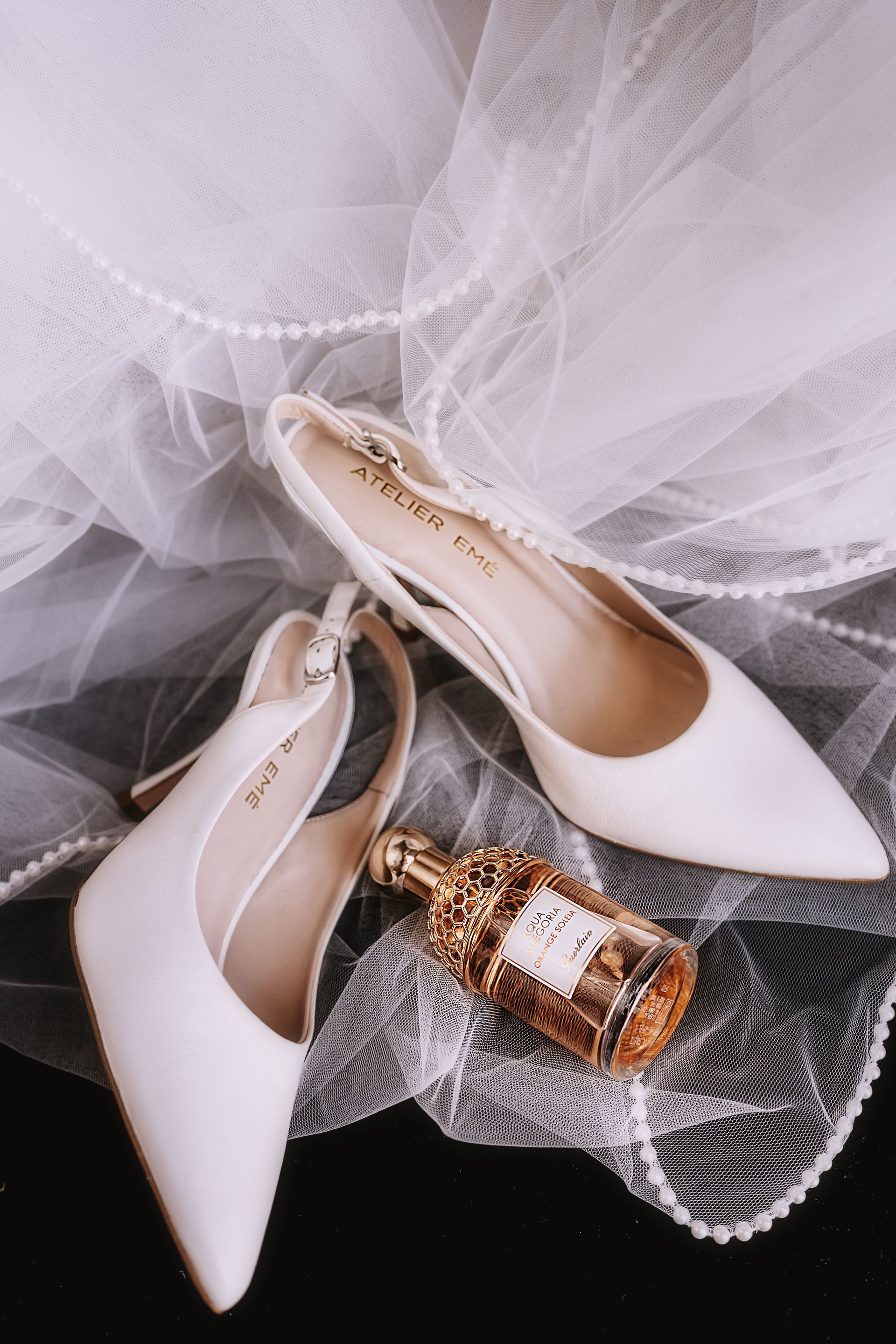 Un paio di scarpe bianche e una bottiglia di profumo su un velo.