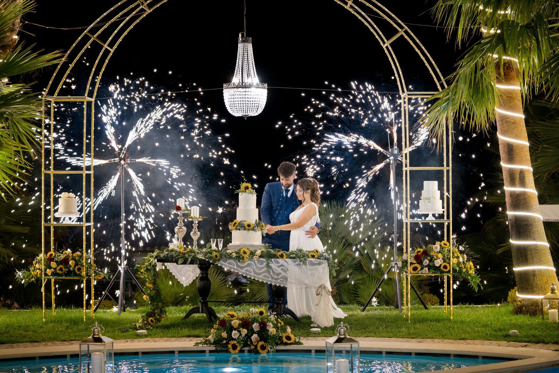 Una coppia di sposi taglia la torta nuziale davanti a uno spettacolo pirotecnico.