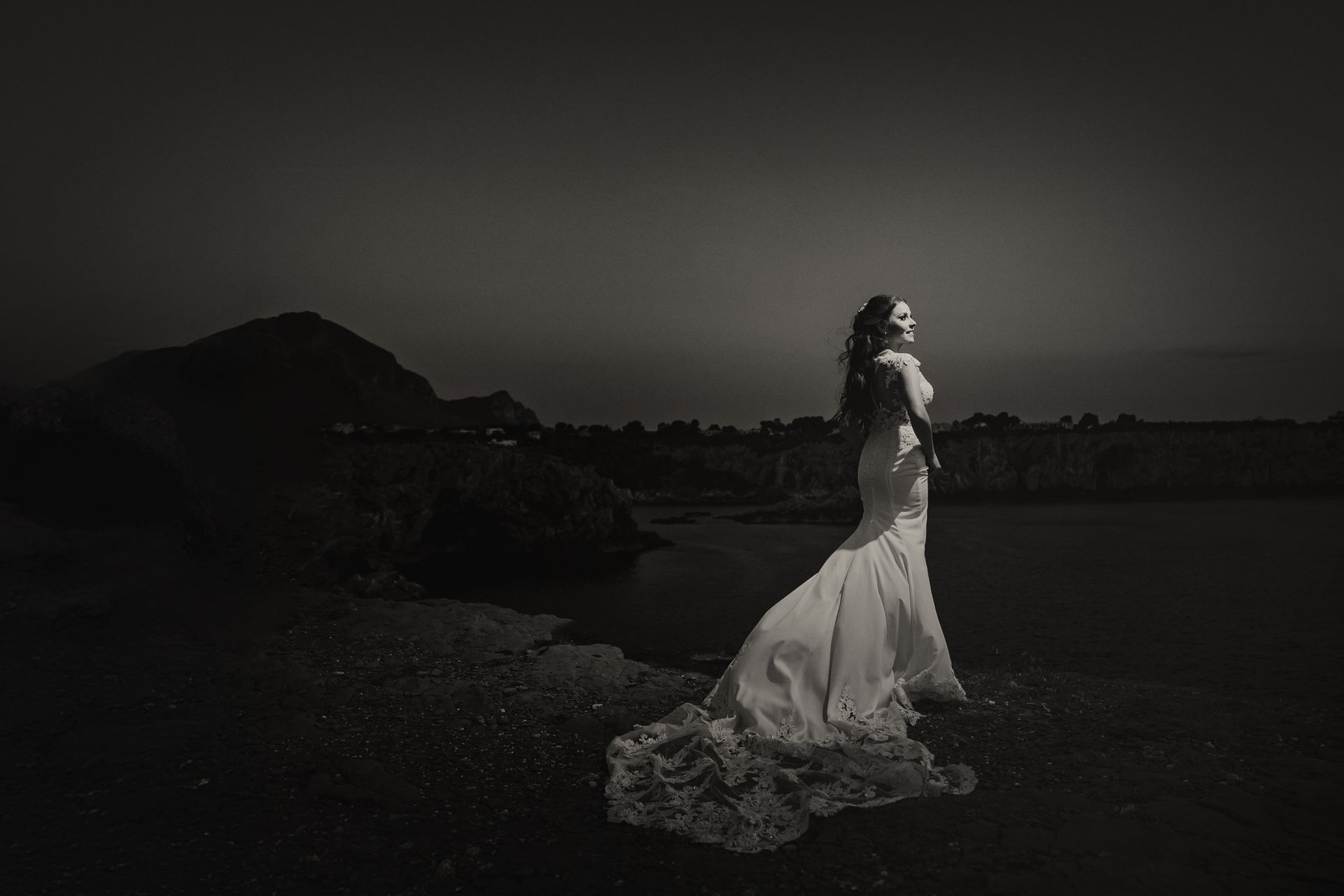 Una foto in bianco e nero di una sposa in abito da sposa in piedi accanto a uno specchio d'acqua.