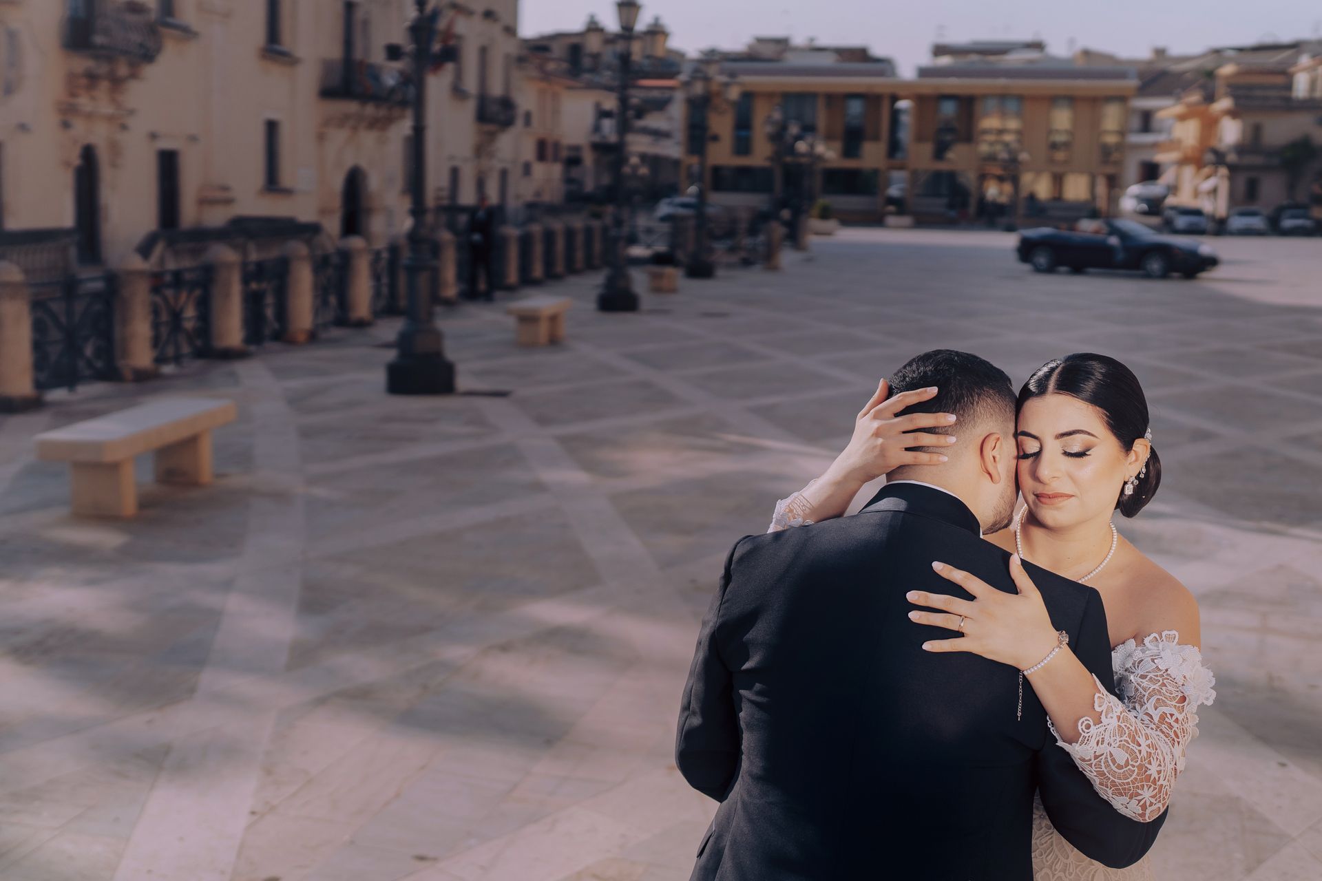 Una sposa e uno sposo si abbracciano in una piazza cittadina.