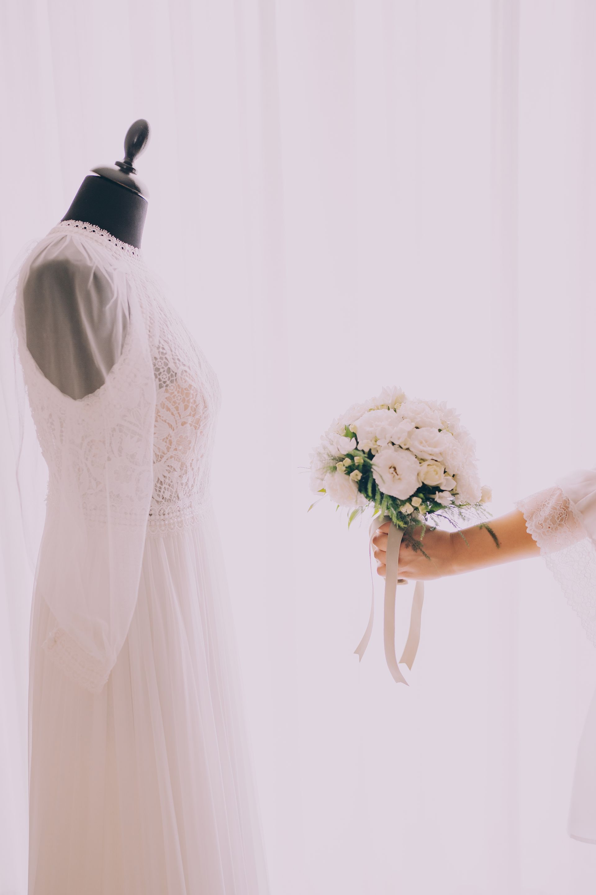 Una donna tiene in mano un mazzo di fiori davanti a un abito da sposa su un manichino.