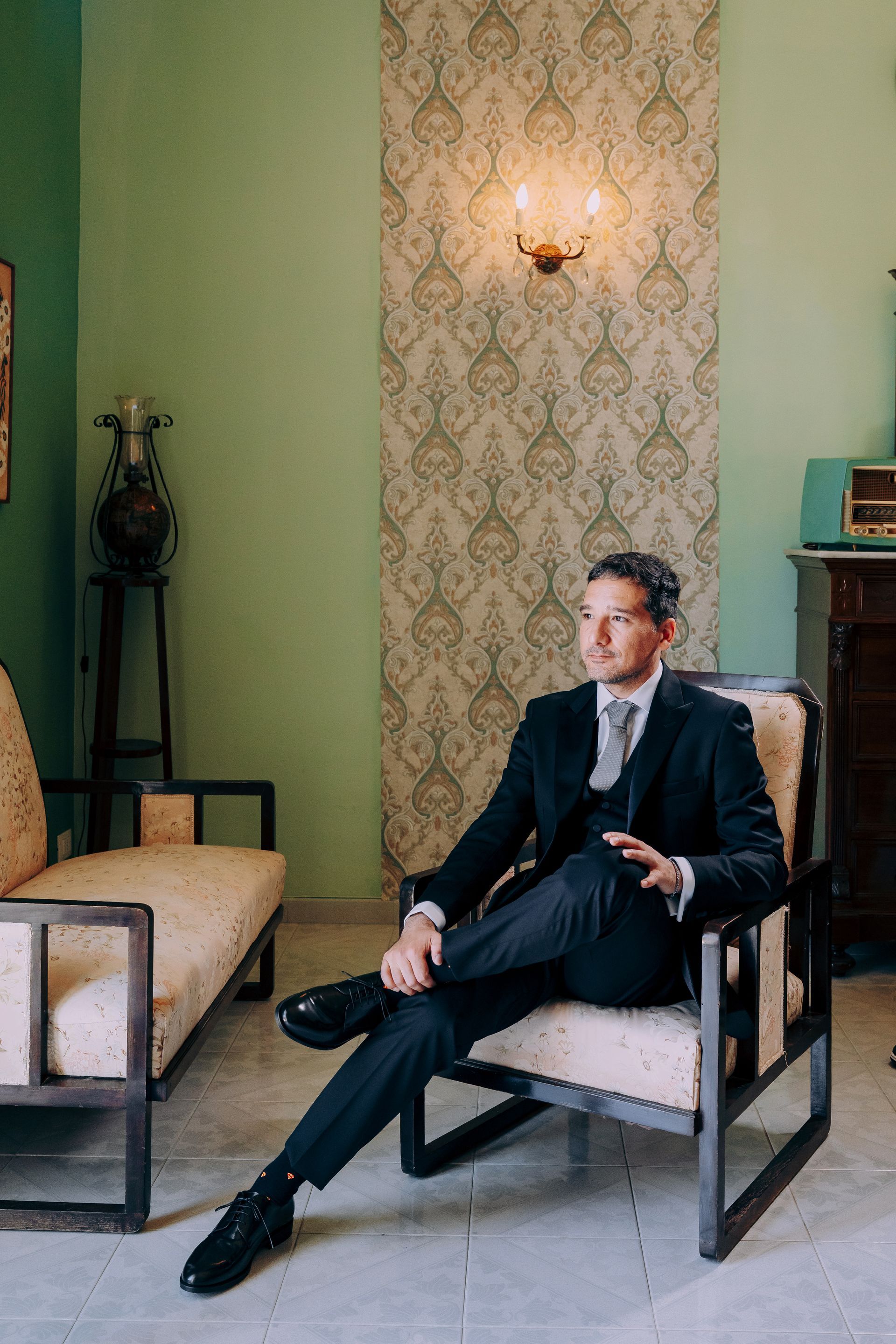 Un uomo in giacca e cravatta è seduto su una sedia in un soggiorno.