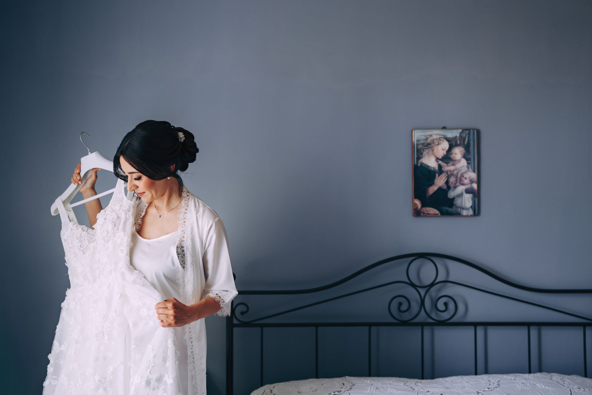 Una donna tiene in mano un abito da sposa davanti al letto.