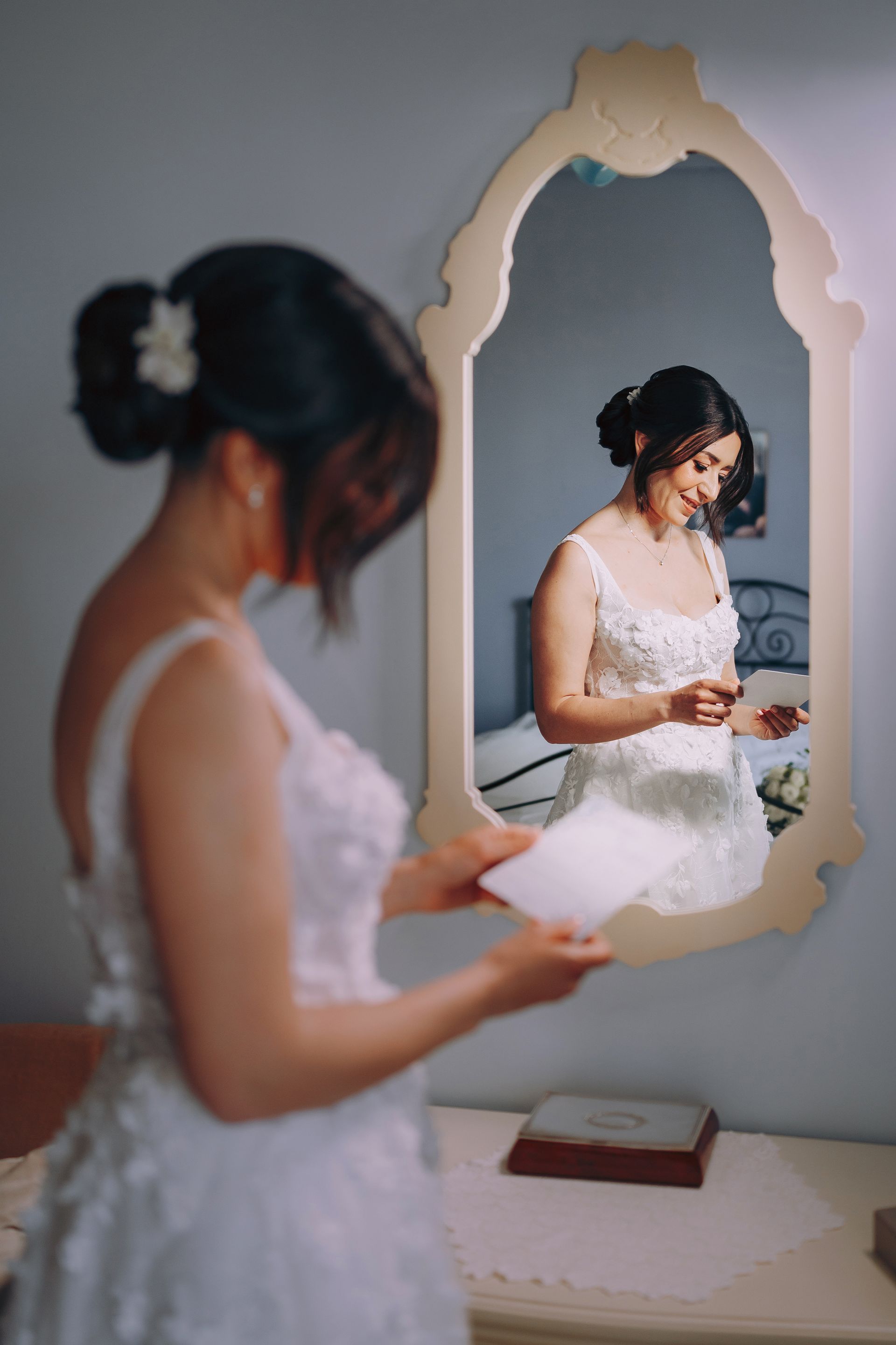 Una donna in abito da sposa legge una lettera davanti a uno specchio.