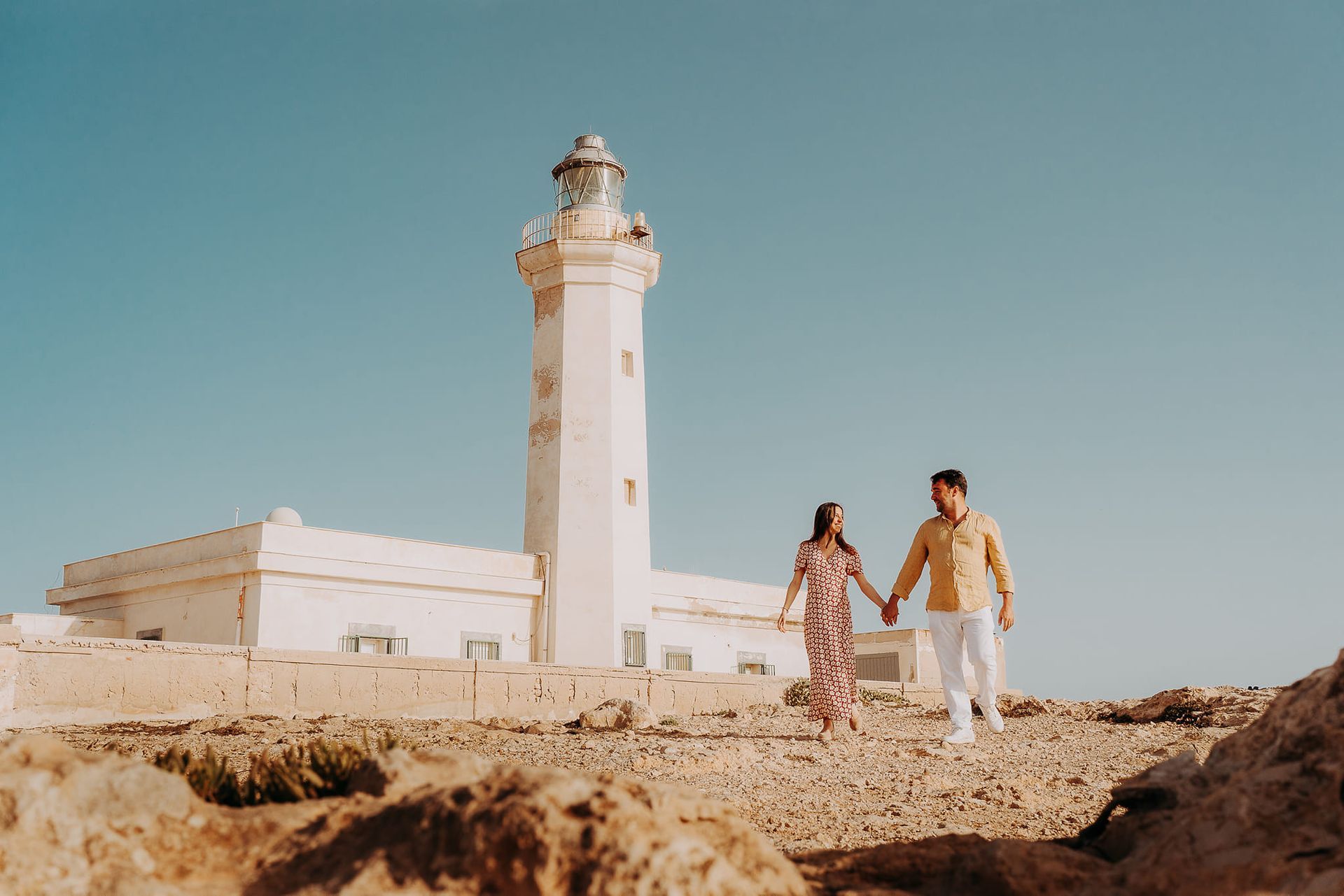 Un uomo e una donna si tengono per mano davanti a un faro.