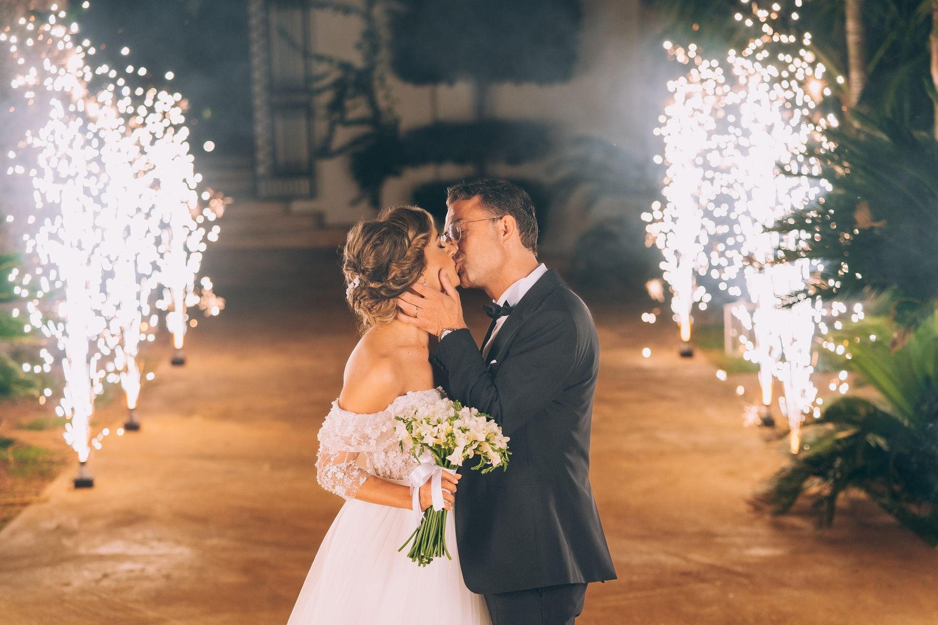 Una sposa e uno sposo si baciano davanti ai fuochi d'artificio.