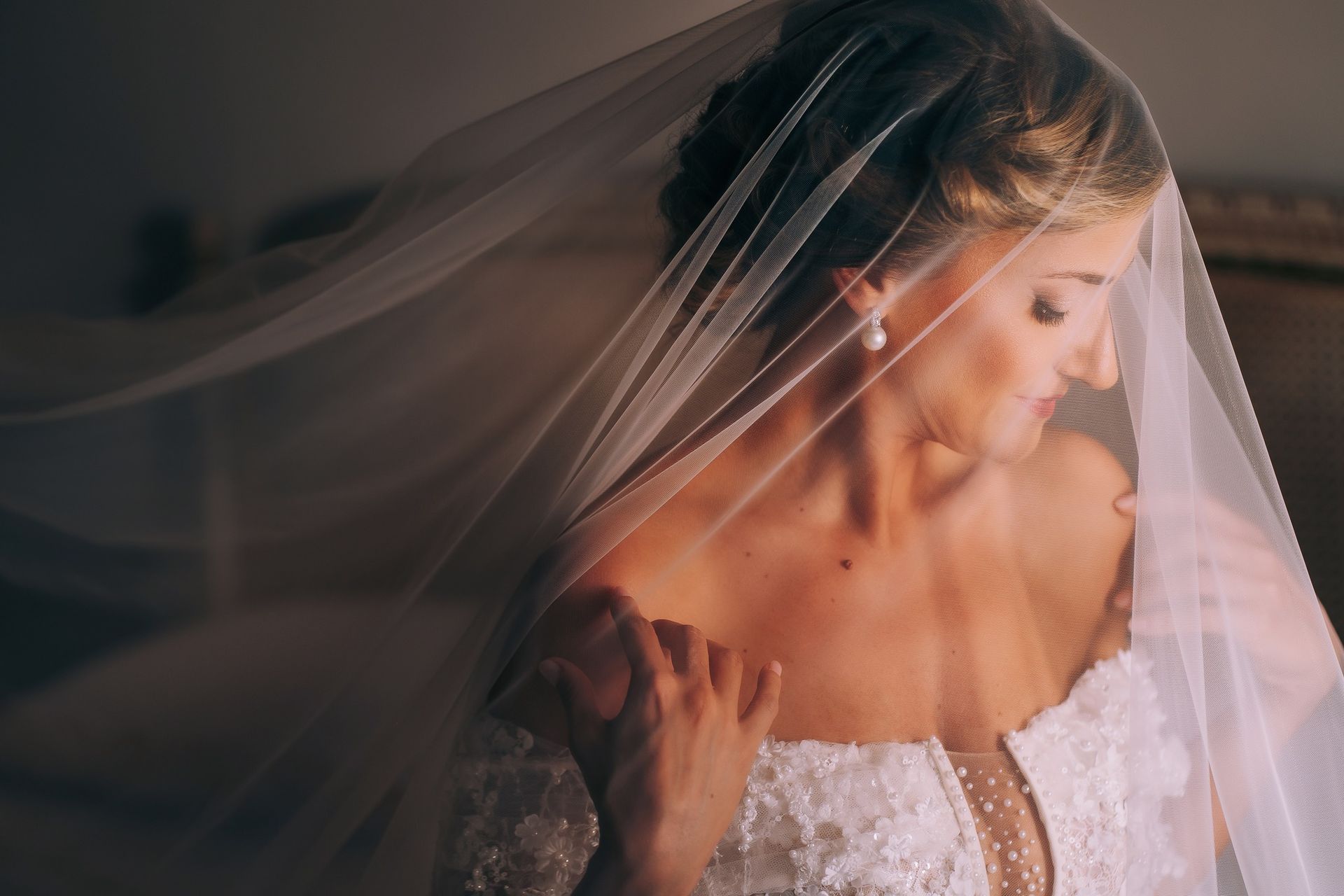 Una donna in abito da sposa e velo è in piedi davanti a una finestra.