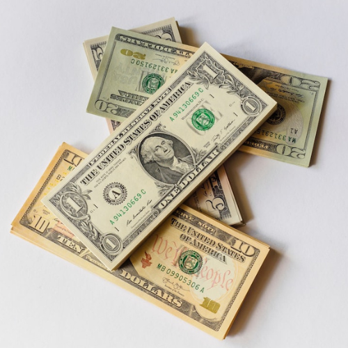 Pile of US dollar bills on white surface. Includes $1, $10, and $20 denominations.