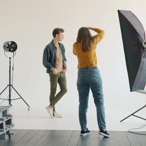 Photographer and model in a studio. The model stands with one hand in pocket, while the photographer adjusts.