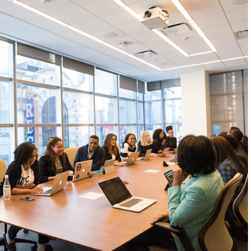 People in a conference room with laptops, windows, and a projector.