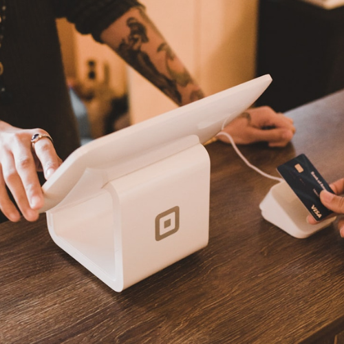 Person swiping a credit card on a white Square payment device at a store counter.