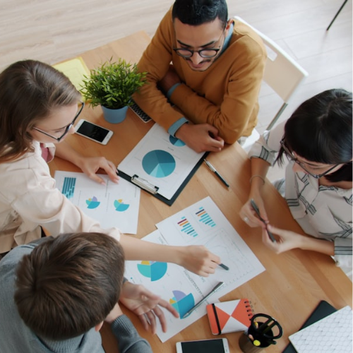 Four people collaborate around a table, reviewing charts and graphs, discussing strategy.