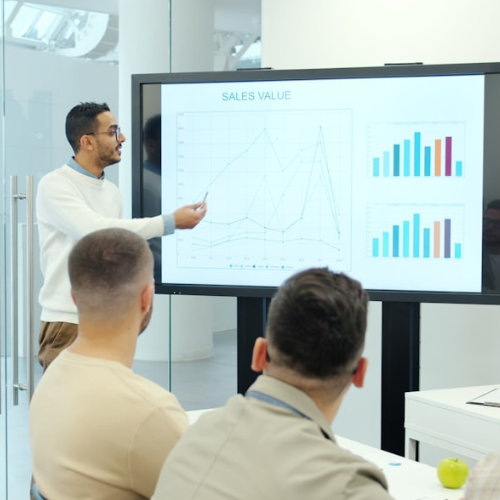 Man giving a presentation to colleagues, pointing at a graph on a large screen.
