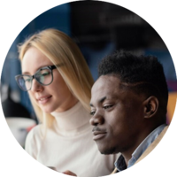 Woman with glasses and Black man look at a screen; both are focused.