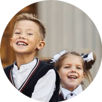 Smiling children in school uniforms, boy in vest, girl with bows, outdoor setting.