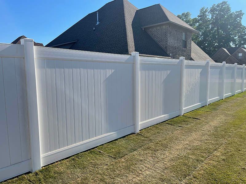 White vinyl privacy fence along a green lawn, with a brick house and blue sky in the background.