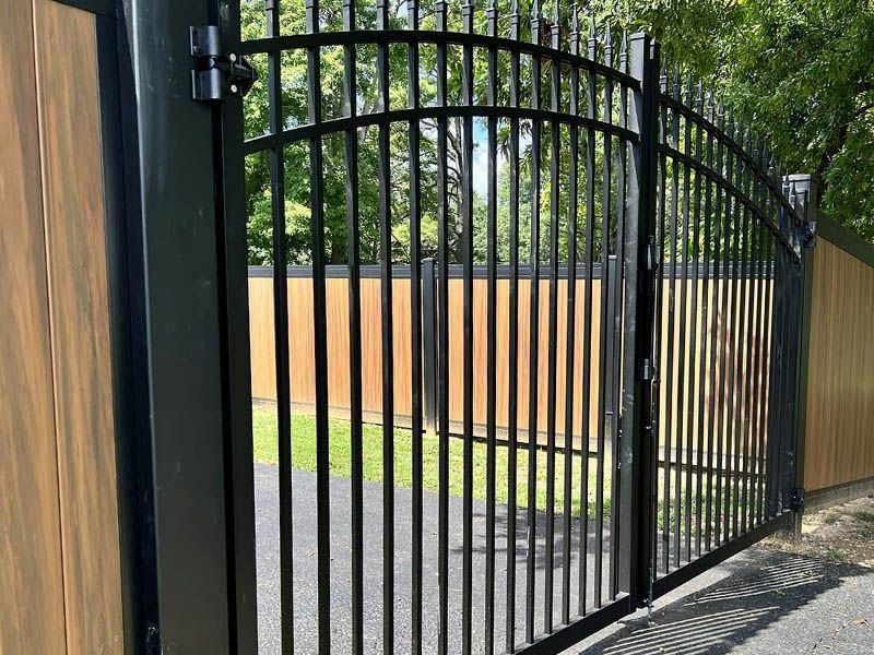 Black metal gate with vertical bars, set in a wooden fence.