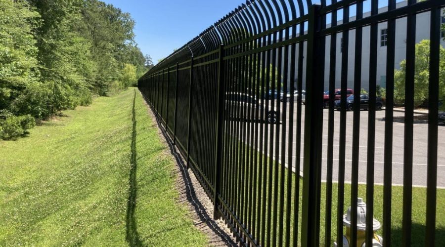 High-security black metal commercial fence with anti-climb curved-top pickets, installed along a par