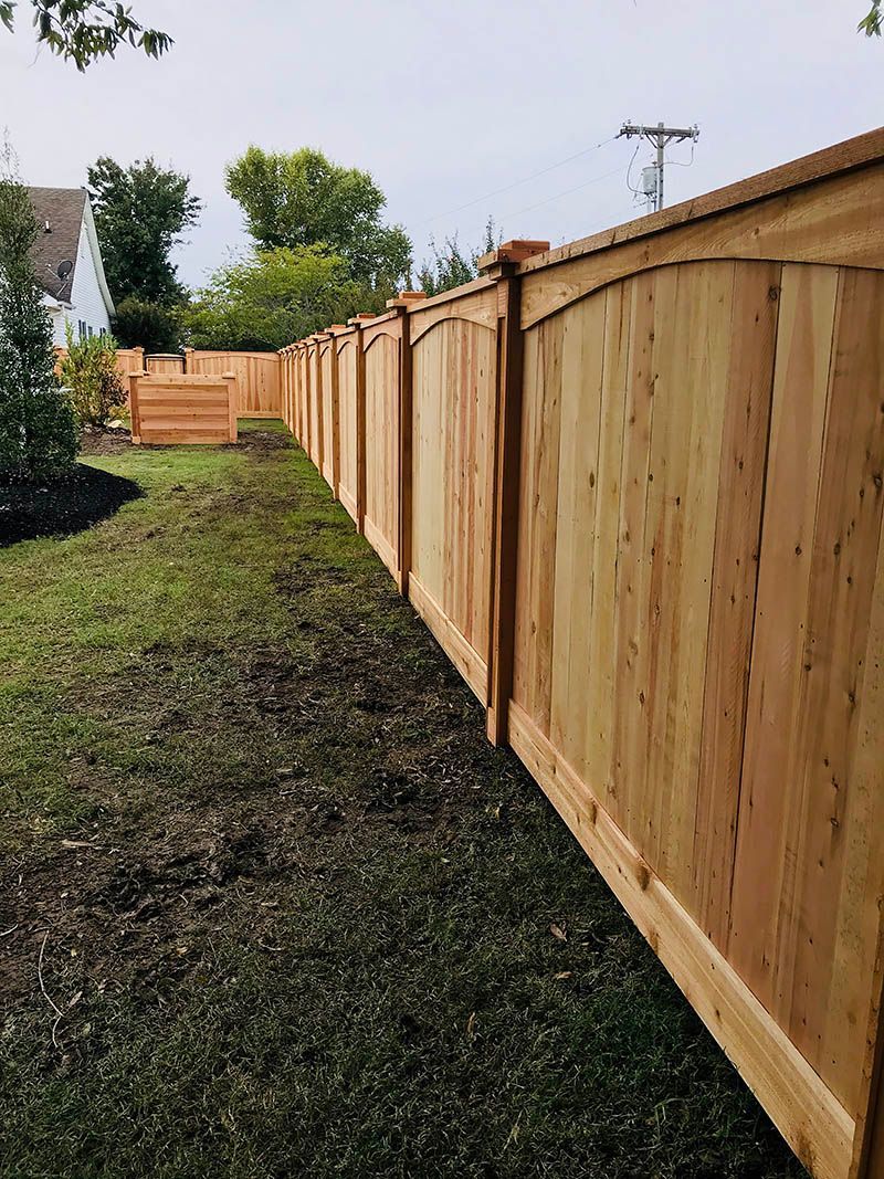 Wooden fence curving along a grassy yard. The fence is light brown with arched panels along the top.