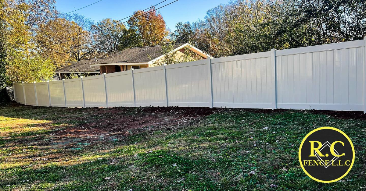 White vinyl fence in a grassy yard, with trees and a house in the background.