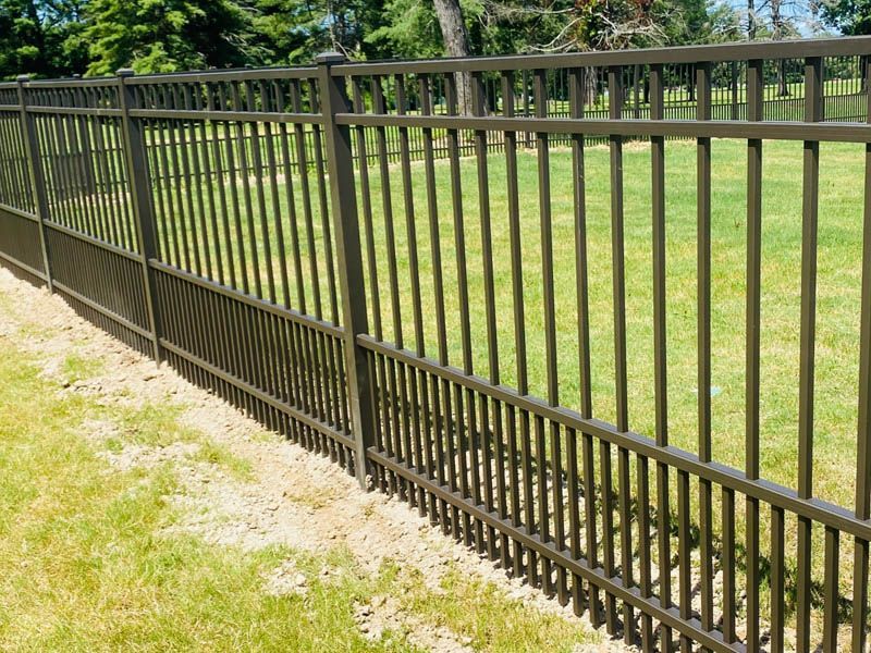 Brown metal fence on a grassy lawn, providing a border to a yard with trees in the background.