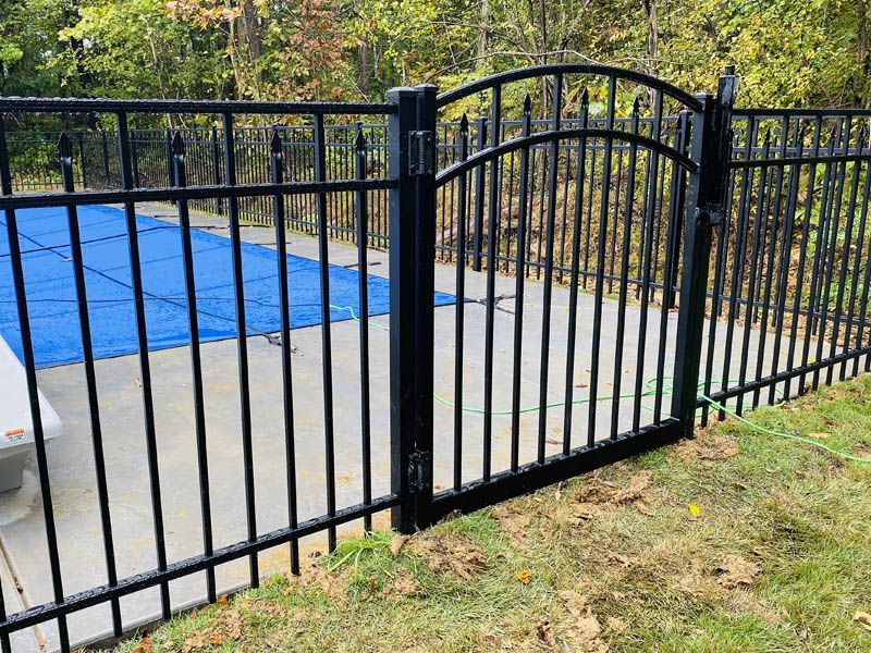 Black wrought-iron fence and gate enclosing a pool area with a blue cover and concrete patio.