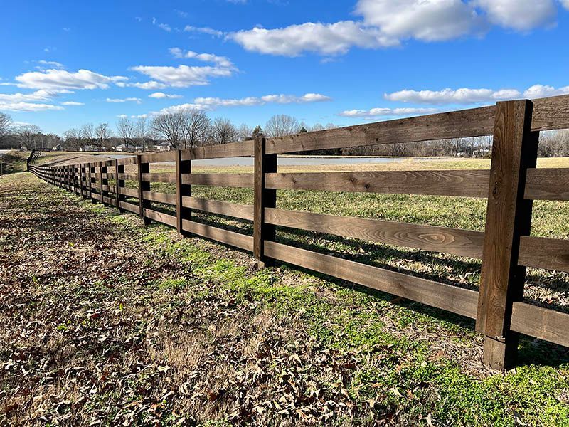 Wooden fence stretches across a grassy field under a partly cloudy blue sky.