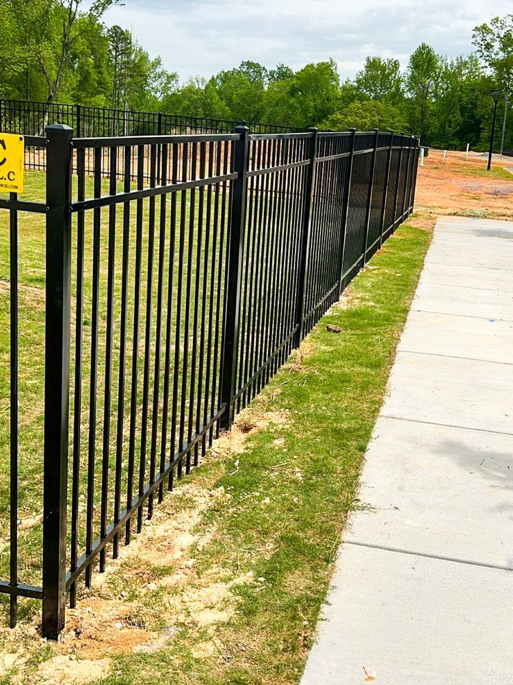 Black metal fence along a sidewalk and grass, with a small portion covered in black mesh for privacy.