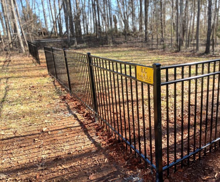 Black metal fence in a yard, with a yellow sign. Trees and dry leaves are in the background.