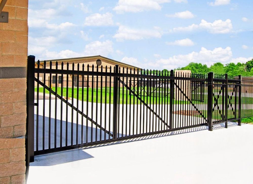 Black metal security gate blocking access to a building with a lawn and cloudy sky.